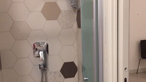 A shower with a glass door, a handheld showerhead, and a wall with hexagonal tiles in various shades. - Apeiron (Corigliano-Rossano)