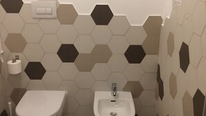 A bathroom with a toilet, bidet, and hexagonal patterned wall tiles. - Apeiron (Corigliano-Rossano)