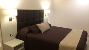 A bedroom with a bed, two bedside tables, and wall-mounted lights. - Apeiron (Corigliano-Rossano)