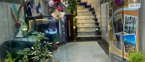 A hotel lobby with a marble floor, a staircase, potted plants, and a Wi-Fi sign.