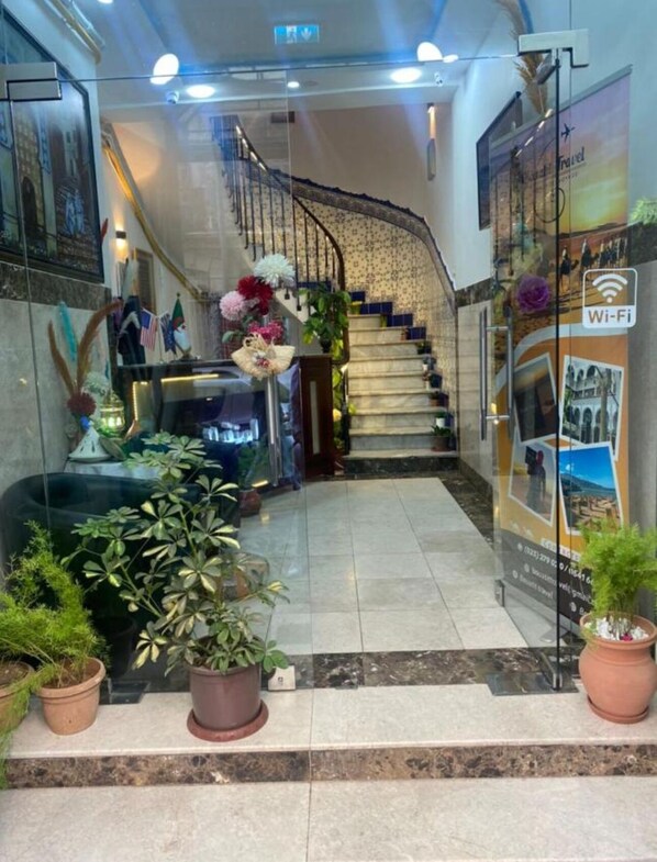 A hotel lobby with a marble floor, a staircase, potted plants, and a Wi-Fi sign. - Afric Hotel Casbah (Algiers)