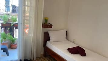 A small, single-bed room with a wooden frame, a white mattress, and a small bedside table with a vase of flowers.