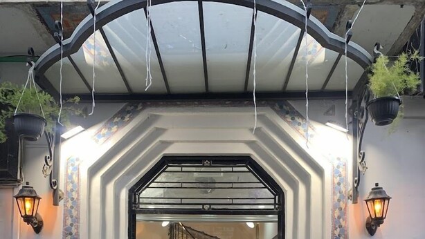 Entrada de un hotel con un toldo de cristal, una escalera que da acceso al interior y plantas en macetas a la entrada.