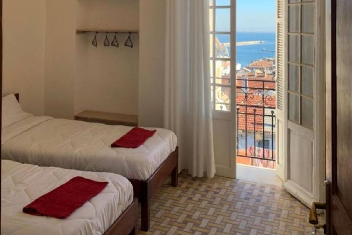 A hotel room with two beds, a view of the sea, and a tiled floor.