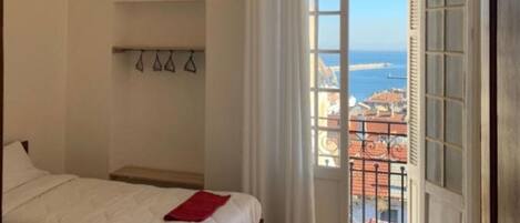 A hotel room with two beds, a view of the sea, and a tiled floor.