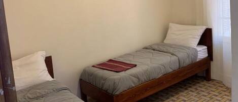 A small, simple room with two single beds, plain walls, and a patterned floor.