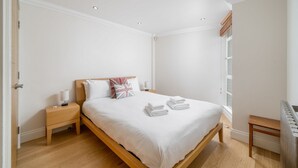Ein Schlafzimmer mit einem hölzernen Bett, weißer Bettwäsche, einem Nachttisch mit Lampe und einem Fenster mit Blick.