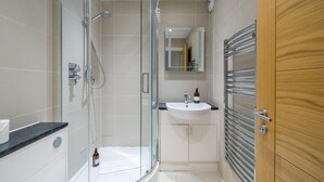 Ein modernes Badezimmer mit einer Duschkabine, einem weißen Waschbecken und einer Holztür.