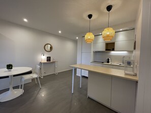 A modern kitchen with a round dining table, white chairs, a small potted plant, and a mirror on the wall.