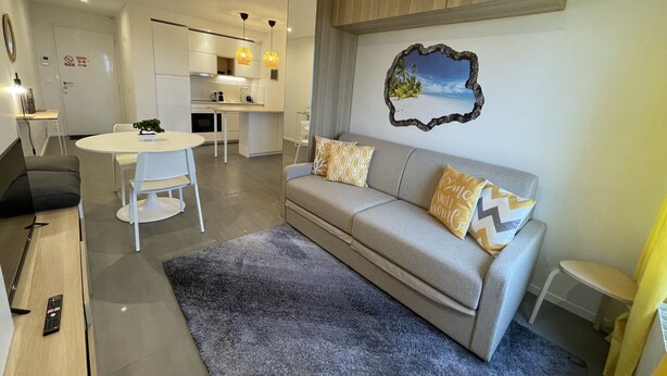 A modern living room with a grey sofa, white dining table, and a kitchen in the background. - Sunset Cocoon T2 46m2 Proche Centre Ville (Villejust)