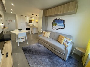 A modern living room with a grey sofa, white dining table, and a kitchen in the background. - Sunset Cocoon T2 46m2 Proche Centre Ville (Villejust)