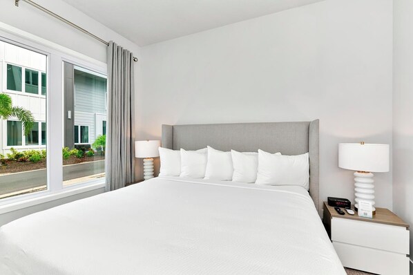 Habitación de hotel con una cama grande, dos mesitas de noche, una ventana con vista a edificios y una cortina gris.