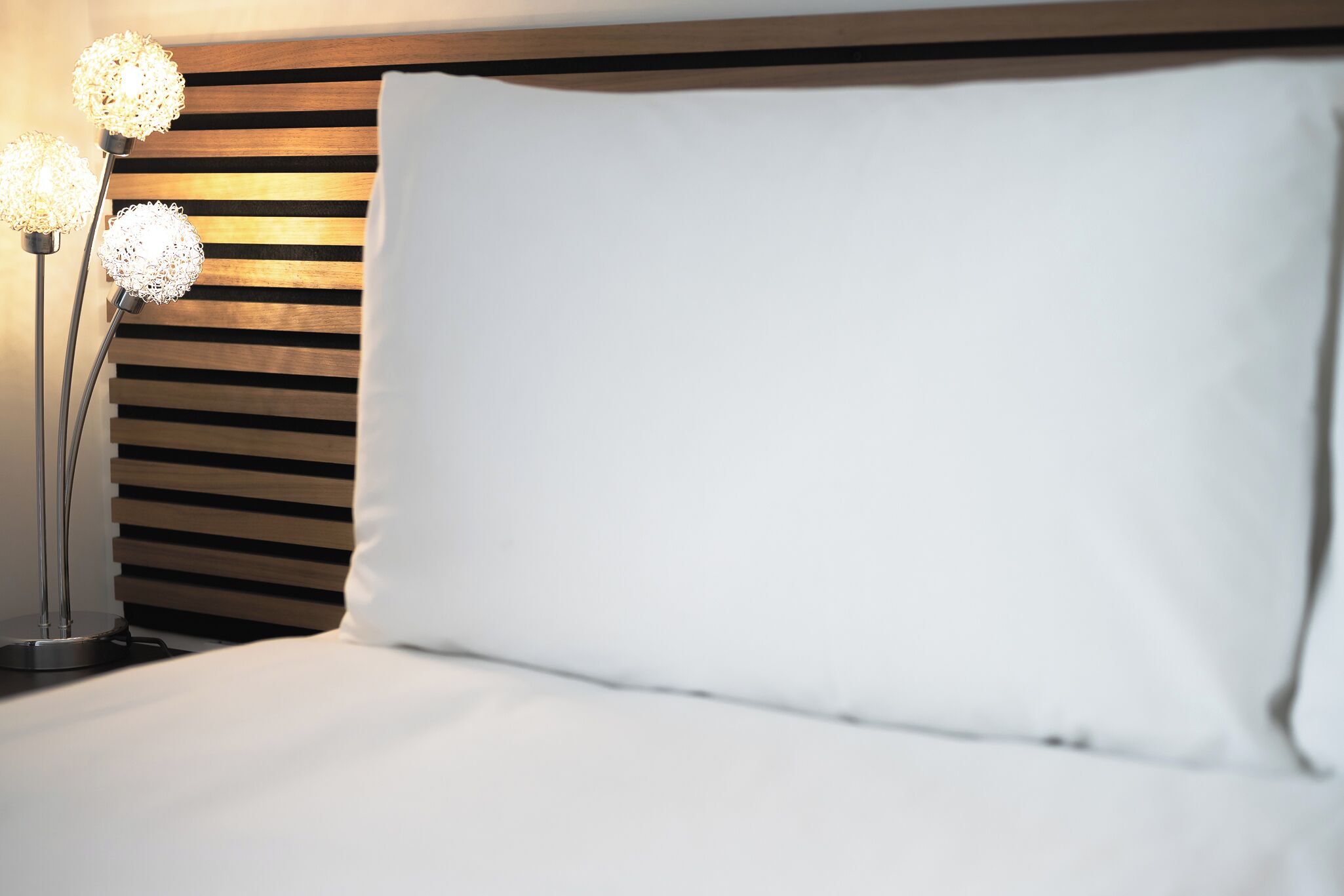 A neatly made bed with a white pillow and a wooden headboard.