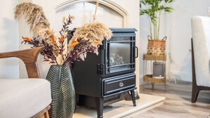 A modern living room with a black wood-burning stove, a decorative vase with dried flowers, and a wicker chair. - Hampshire Charming House (Lincoln)