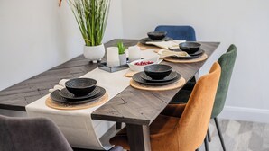 A dining table set with black bowls, plates, and a white placemat. There are chairs around the table, and a vase with green plants on the side. - Hampshire Charming House (Lincoln)
