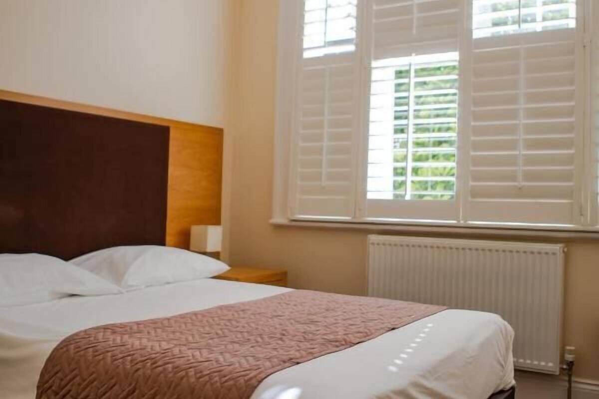 A bedroom with a bed, a window with shutters, and a radiator.