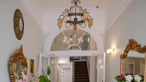 En storslagen hall med en kristallkrona, utsmyckade speglar och en öppen spis.