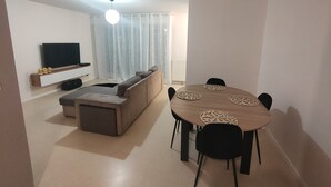 Moderni olohuone, jossa on sohva, televisio ja ruokapöytä tuoleineen.