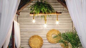 A rustic spa area with a wooden bench, two large woven wall decorations, a hanging fern, and a doormat with text. - Chalés Magia do Campeche  (Florianópolis)