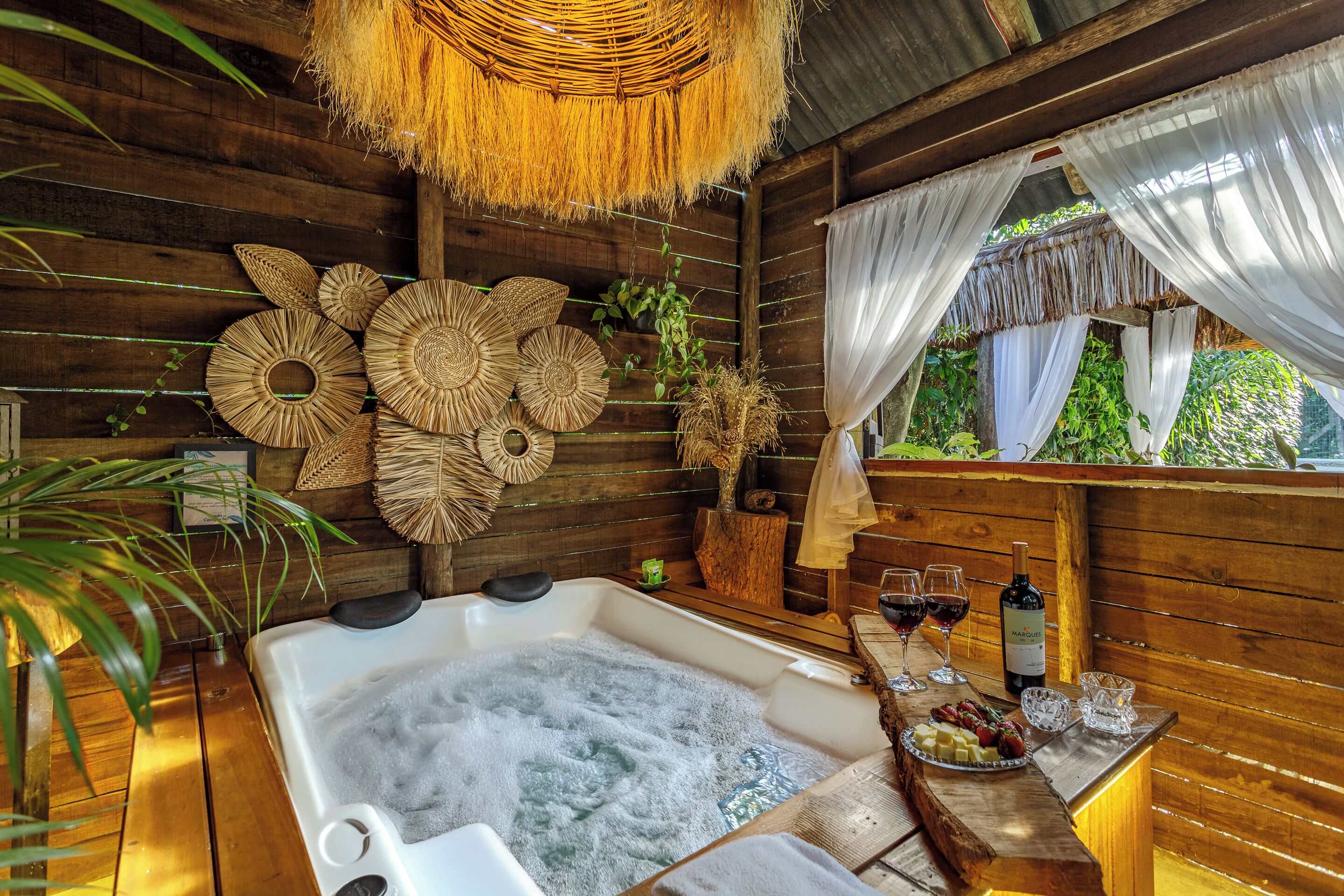A wooden cabin with a hot tub, wicker wall decor, and a table with wine glasses and snacks.