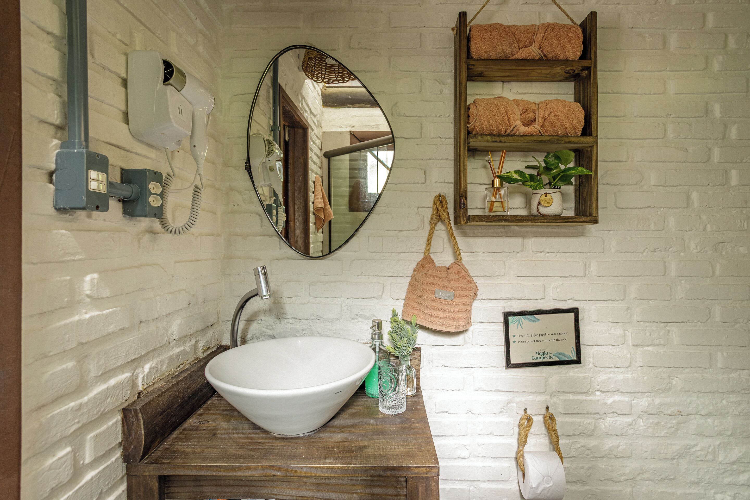 A bathroom with a white sink, a mirror, a towel rack, and a shelf with towels.