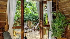 A wooden cabin with a large bathtub, a dining table with food and drinks, and a view of the garden outside. - Chalés Magia do Campeche  (Florianópolis)