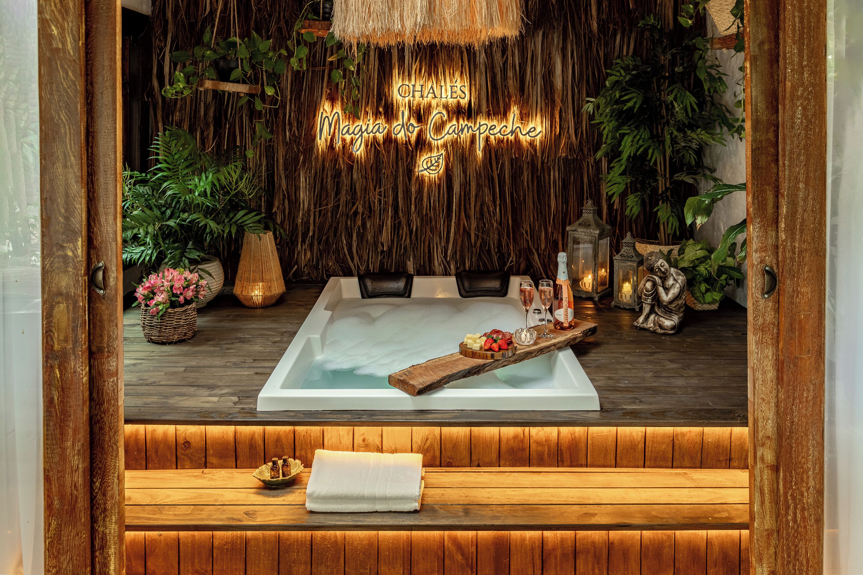 Un área de spa con un jacuzzi, suelo de madera y una pared decorada con plantas colgantes.