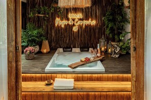 A spa area with a hot tub, wooden flooring, and a wall with hanging plants. - Chalés Magia do Campeche  (Florianópolis)