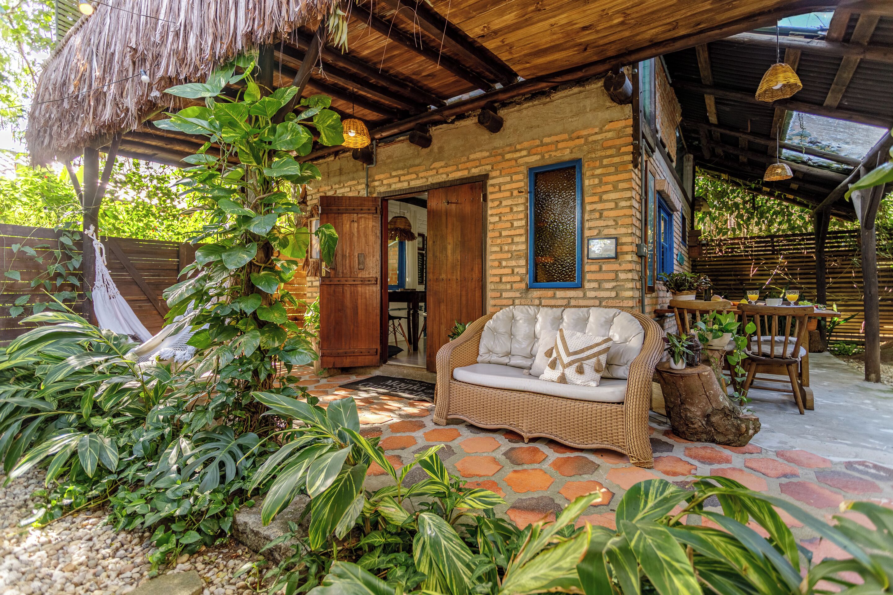 A cozy outdoor seating area with a wicker sofa, a thatched roof, and lush greenery.