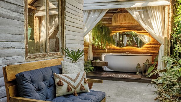 A rustic cabin with a wooden bench, a bathtub, and a window overlooking greenery. - Chalés Magia do Campeche  (Florianópolis)