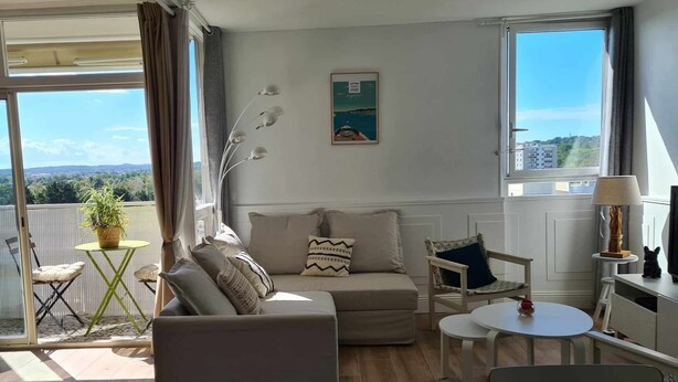 Ett modernt vardagsrum med en soffa, ett litet bord och en stol. Det finns en balkong med utsikt över staden.