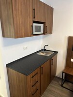 Una cocina compacta con armarios de madera, encimera negra, pileta de acero inoxidable y microondas.