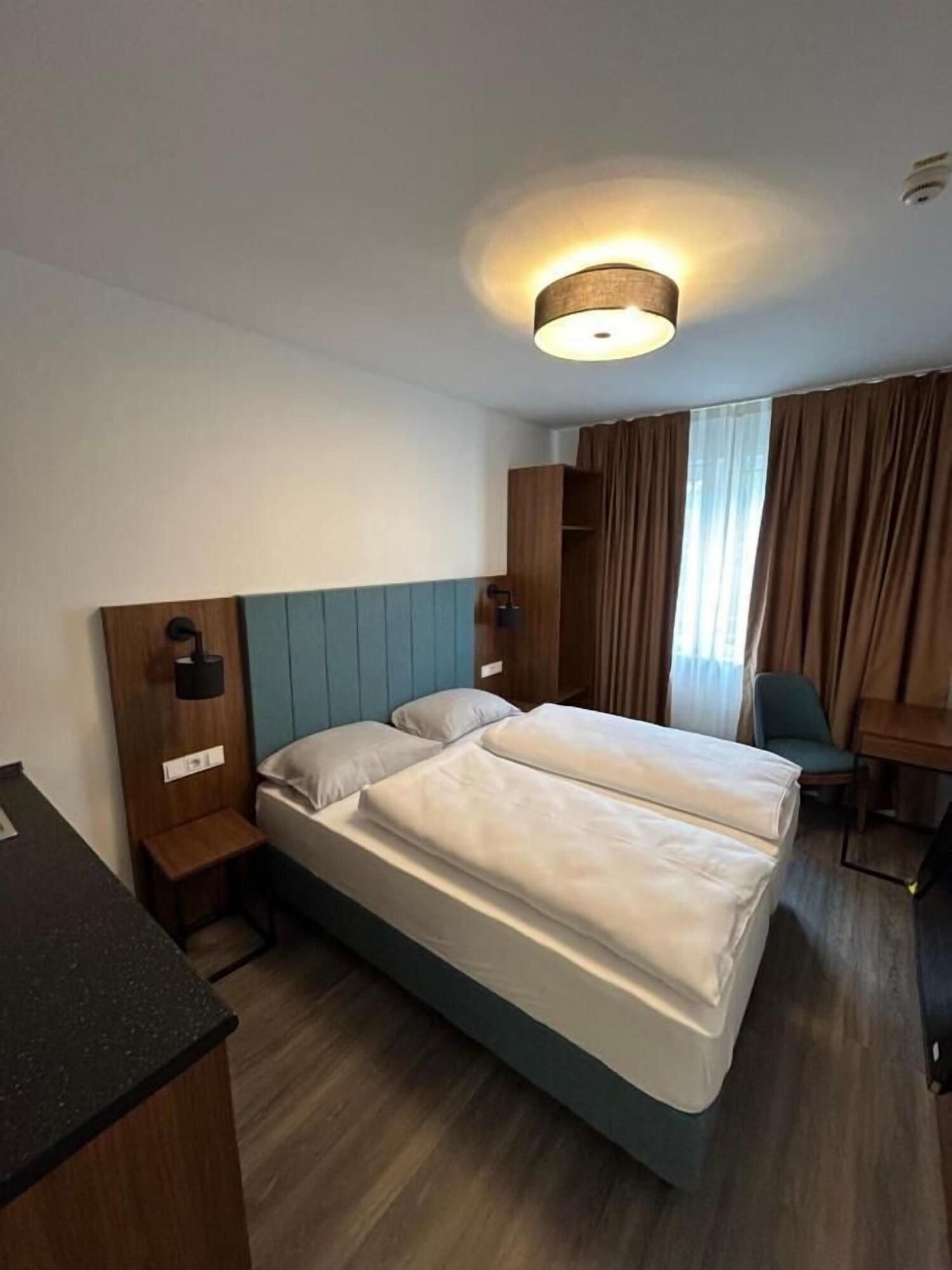 Ein Hotelzimmer mit zwei Betten, einem Schreibtisch, einem Stuhl, einem Kleiderschrank und einer Deckenleuchte.