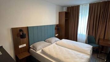 Ein Hotelzimmer mit zwei Betten, einem Schreibtisch, einem Stuhl, einem Kleiderschrank und einer Deckenleuchte.