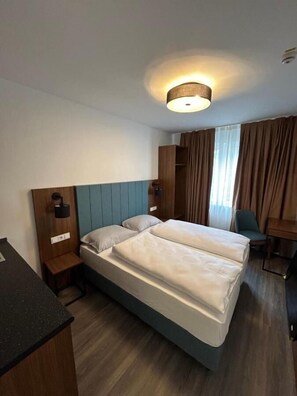 A hotel room with two beds, a desk, a chair, a wardrobe, and a ceiling light. - Munique Hotel Unterschleißheim (Unterschleissheim)