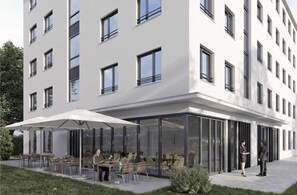 A modern building with a flat facade, multiple windows, and a covered outdoor seating area with tables and chairs. - Munique Hotel Unterschleißheim (Unterschleissheim)