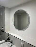 Un baño moderno con un espejo redondo, un lavabo blanco y una zona de ducha.