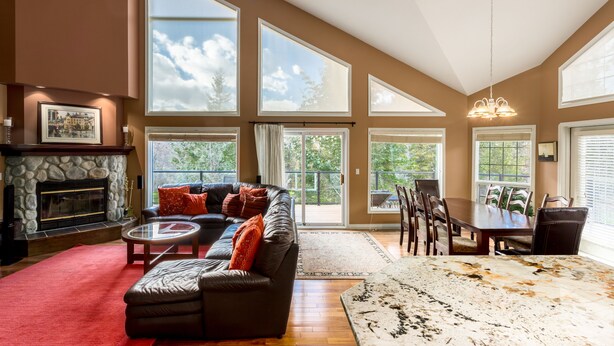 A spacious living room with a fireplace, large windows, a ceiling fan, and a dining area with a table and chairs.