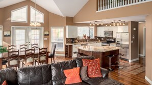 A spacious living area with a black leather sofa, a dining table with chairs, and a kitchen with a central island.