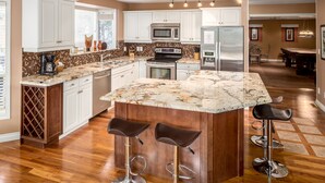 A kitchen with white cabinets, a large island with stools, a microwave, a stove, and a refrigerator.