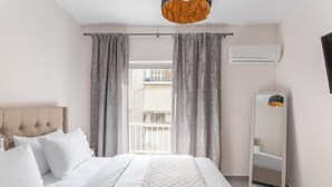 A hotel room with a bed, a large mirror, and a window with curtains. - Afroditi Suite (Nea Smirni)