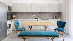 A modern kitchen with a wooden table, two blue upholstered chairs, and a bench. - Afroditi Suite (Nea Smirni)