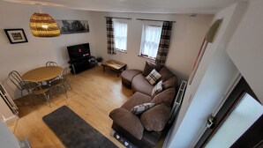 A living room with a sofa, a dining table with chairs, a TV, and a hanging light fixture. - Heart of Lincoln City, 3 Bedrooms, Sleeps 4 Guests (Lincoln)