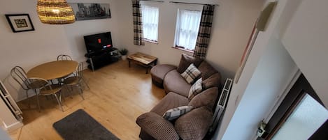Una sala de estar con sofá, una mesa de comedor con sillas, un televisor y una lámpara colgante.