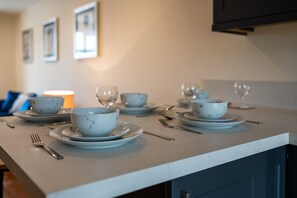 A dining table set with white bowls and plates, silverware, and wine glasses.