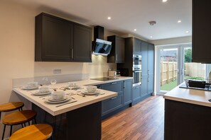 A modern kitchen with dark cabinets, a central island with seating, and a large window providing a view of the backyard. - Beautiful Brand new Build 2-bedroom House Sleeps 5 (Lincoln)