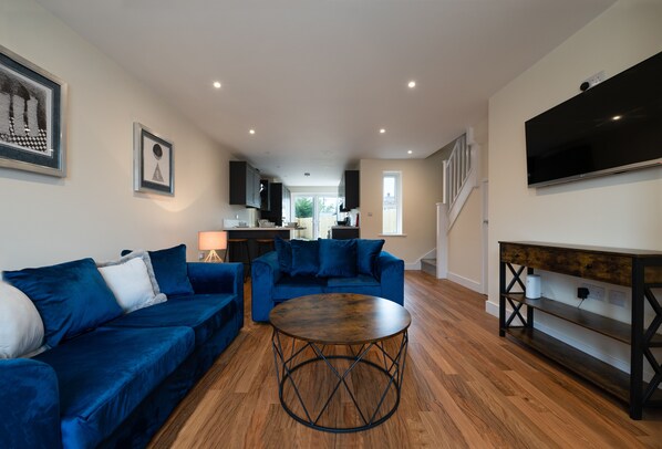 A modern living room with a blue sofa set, a round coffee table, and a TV mounted on the wall.