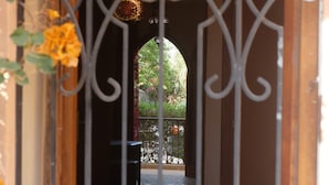 Um corredor interno com um portão de metal, um banco coberto e vista de um jardim através de um arco.