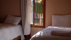 Quarto com duas camas de solteiro, uma janela com vista para árvores e uma cortina.