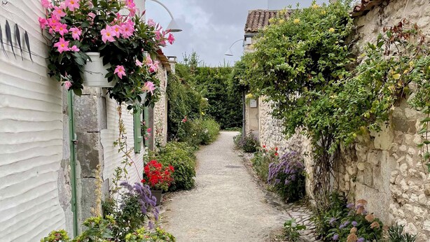 A narrow cobblestone path flanked by buildings with hanging flowers and a sign for 'ARÔMES'. - Charming appartment in the heart of La Palmyre (Les Mathes)